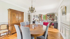 Un comedor con una mesa de madera, seis sillas, una araña, un aparador grande de madera y una estantería al fondo.