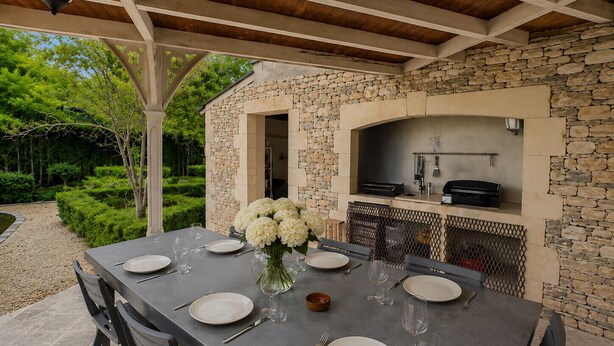 Un área de comedor al aire libre con un muro de piedra, un arco y una estación de parrillada.