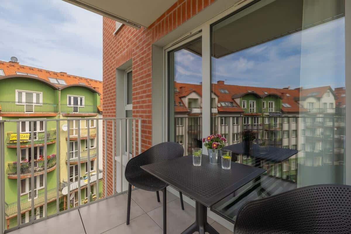 Un balcón con mesa y sillas, una puerta de cristal y vistas a edificios cercanos.