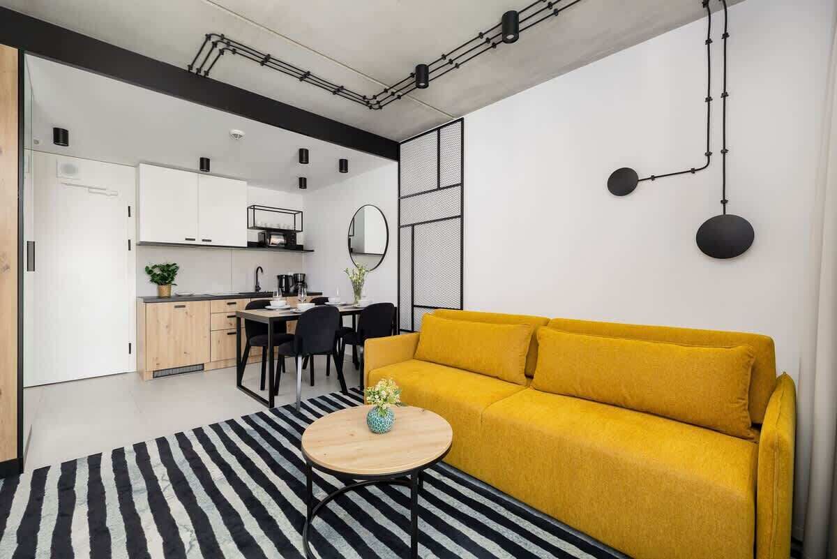 Living room featuring a mustard-yellow sofa, black accents, and a round coffee table on a striped rug.


