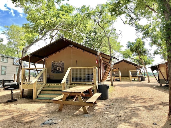 A campsite with wooden cabins, picnic tables, and a fenced area.