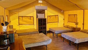 Uma tenda com três camas, uma cafeteira e uma pequena mesa.