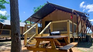 Uma cabana de madeira com varanda coberta, mesa de piquenique e churrasqueira.