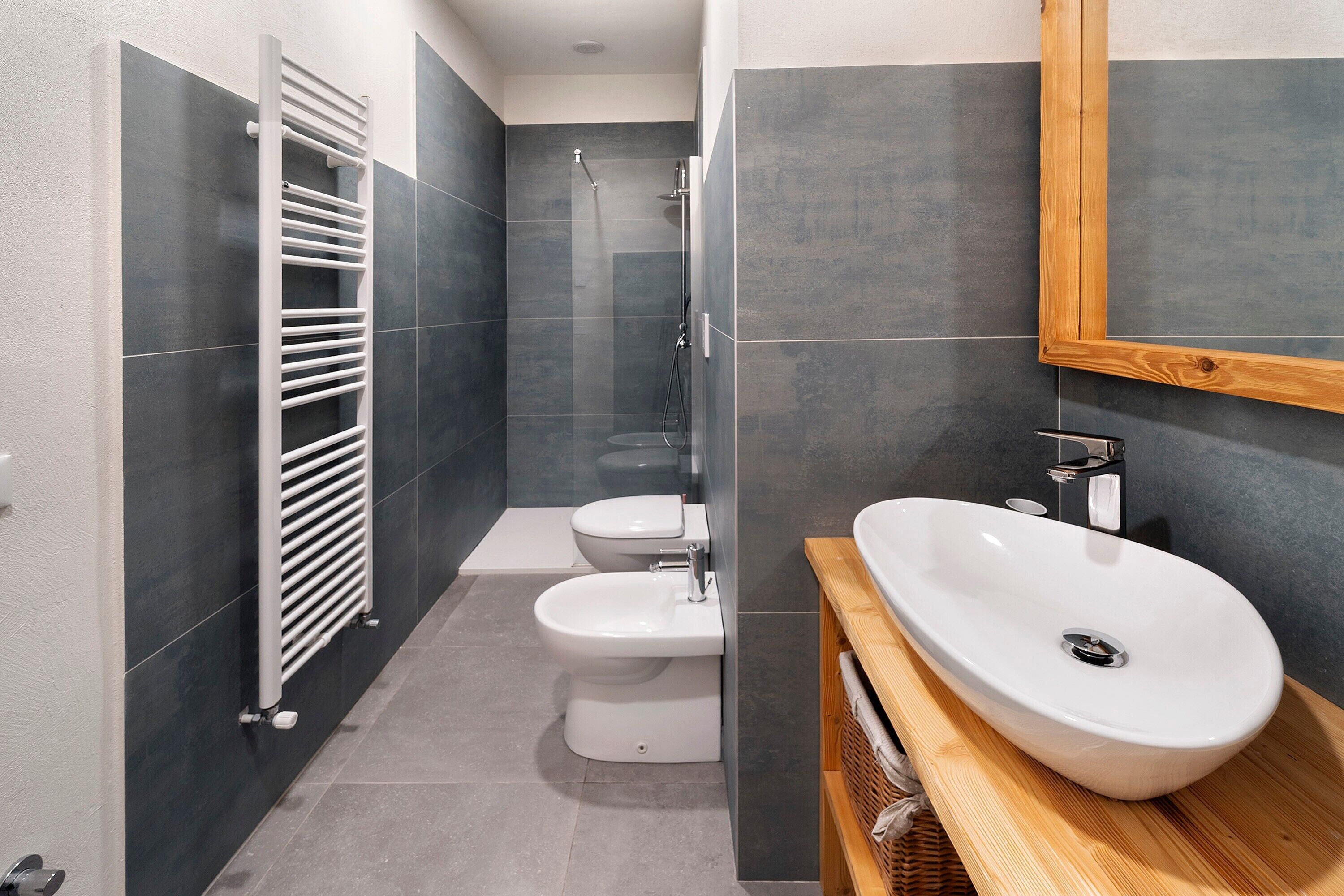 A modern bathroom with a white toilet, a bidet, a white sink, and a wooden vanity.