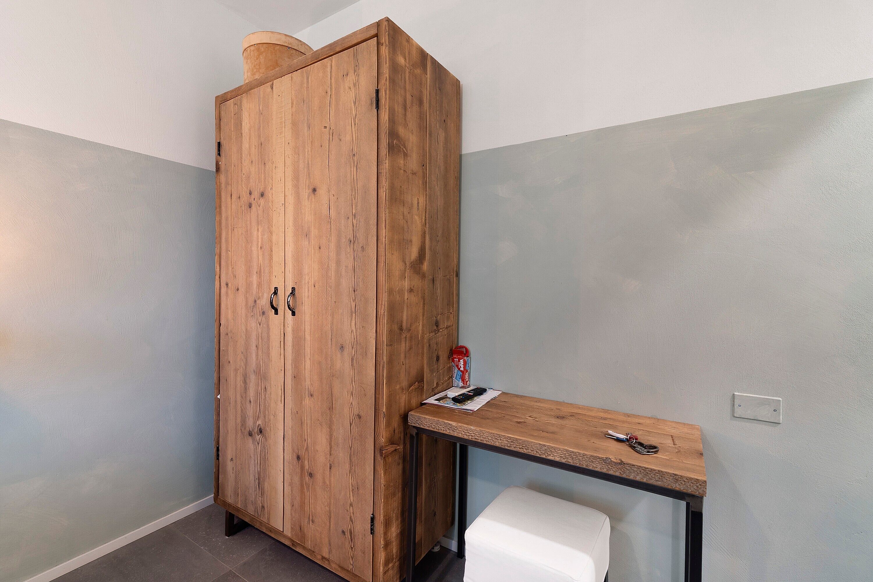 A wooden wardrobe with a small table beside it, a white bench, and a light switch on the wall.