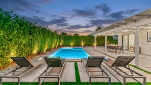 A swimming pool with lounge chairs, a covered patio area, and a hedge. - Desert Oasis w/ Pool & Spa, Game Room + Theater (Indio)