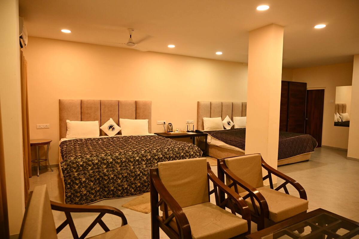 A hotel room with two beds, a desk, chairs, and a ceiling fan.