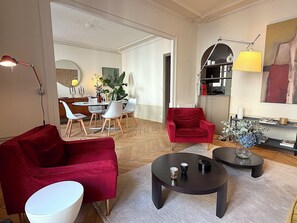 Ein Wohnzimmer mit einem roten Sofa, einem weißen runden Tisch, einem schwarzen Couchtisch und einem Essbereich mit Tisch und Stühlen.
