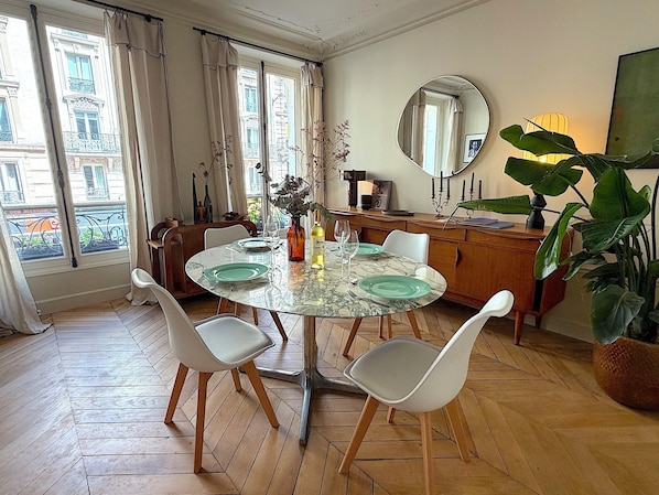Ein Essbereich mit einem runden Tisch, weißen Stühlen, einem Spiegel und einem Blumentopf.