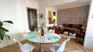 Ein Essbereich mit einem Marmortisch, zwei weißen Stühlen und einer Vase mit getrockneten Blumen.
