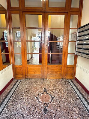 Eine Holztür mit doppelten Flügeln und Glasscheiben, ein strukturierter Boden und eine Treppe im Hintergrund.