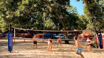 A beach volleyball game with tents and cars in the background.