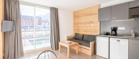 A modern room with a sofa, a dining table, a TV, a kitchen area, and a view of buildings.