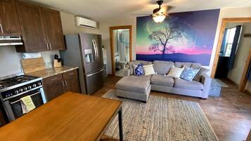 A modern kitchen with a dining area, a gray sofa, and a large painting of a tree.