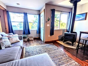 A living room with a sofa, a rug, a fireplace, and large windows with curtains. - California Lakeview Escape: Santa Ysabel Glamping to Recharge (Santa Ysabel)