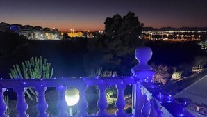 Vista nocturna de un balcón con barandilla, una piscina y un paisaje urbano al fondo.