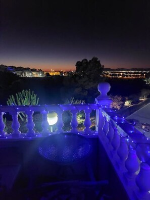 A night view of a balcony with a railing, a pool, and a cityscape in the background. - Casa Helgar in Gran Alacant, Beautiful Sun Set Views & Perfectly Located (Santa Pola)