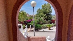 Vista a través de un arco con un farol, plantas variadas y una barandilla blanca.