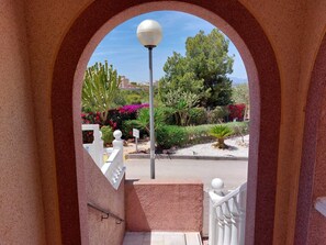 A view through an arched doorway with a street lamp, various plants, and a white railing. - Casa Helgar in Gran Alacant, Beautiful Sun Set Views & Perfectly Located (Santa Pola)