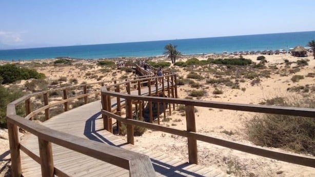 Un paseo marítimo de madera que conduce a una playa, bajo cielos despejados.