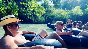 People floating on water in tubes, surrounded by greenery.