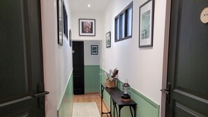 A hallway with a wooden floor, a rug, a table with plants, and framed pictures on the walls.