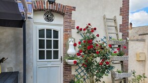 A white door with a window, a brick wall, a white vase with red roses, and a wooden ladder.