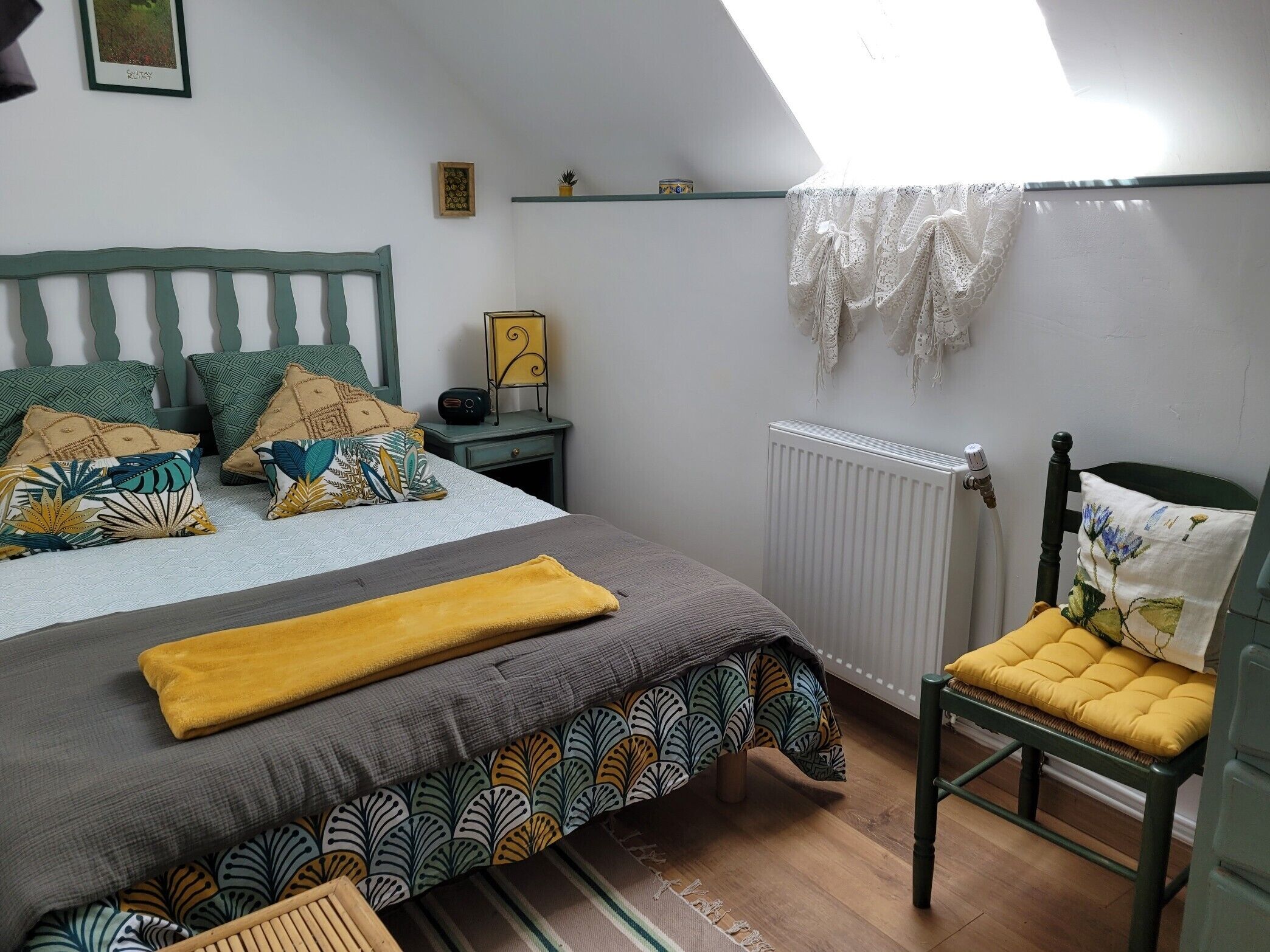 Een slaapkamer met een bed, een stoel, een radiator, een plank en een raam.