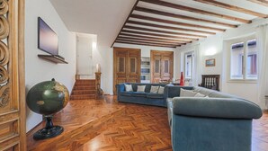 Amplia sala de estar con piso de madera en patrón chevron, un sofá azul, un globo terráqueo y armarios de madera.