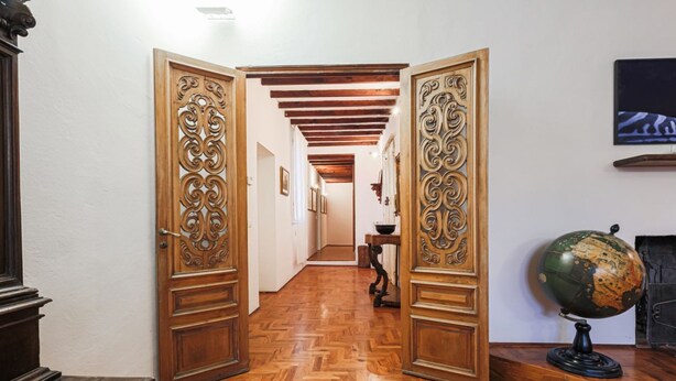 Un pasillo con suelo de madera, puertas ornamentadas, un globo terráqueo y una chimenea.