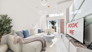 Uma sala de estar moderna com sofá, mesa de centro e uma TV exibindo 'BOOK ME'.