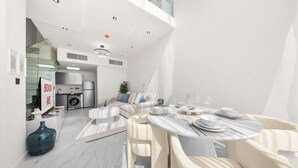 Cozinha moderna com armários brancos, uma máquina de lavar e uma sala de jantar com uma mesa redonda para quatro pessoas.