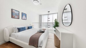 Quarto moderno com cama, mesa de cabeceira, espelho e varanda com vista.