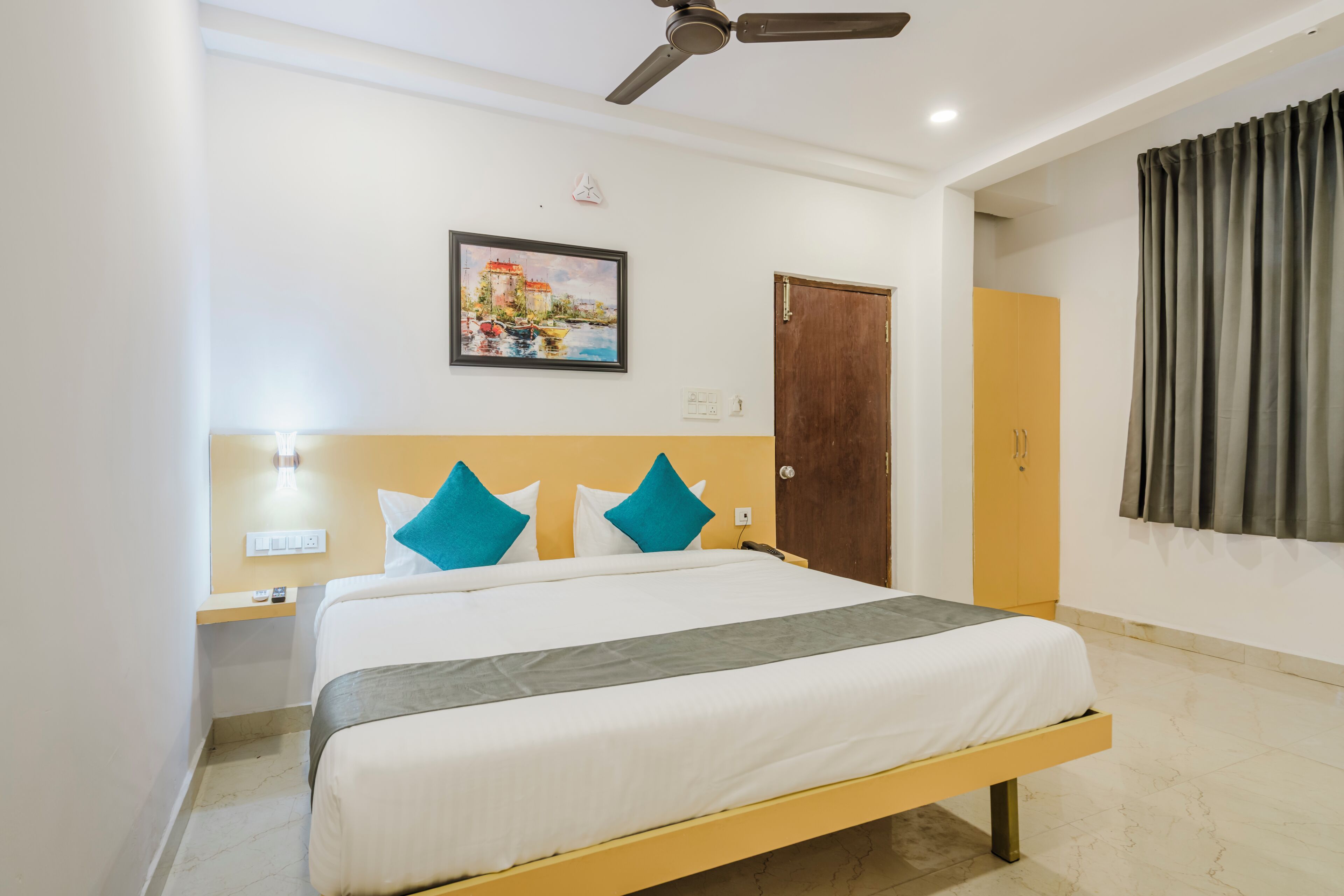 Une chambre d’hôtel avec un lit, un ventilateur de plafond, un tableau, une armoire et un rideau.