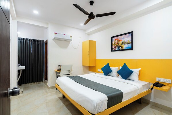Une chambre d’hôtel avec un lit, un ventilateur de plafond, une table de chevet avec un téléphone, un climatiseur fixé au mur et un tableau au mur.