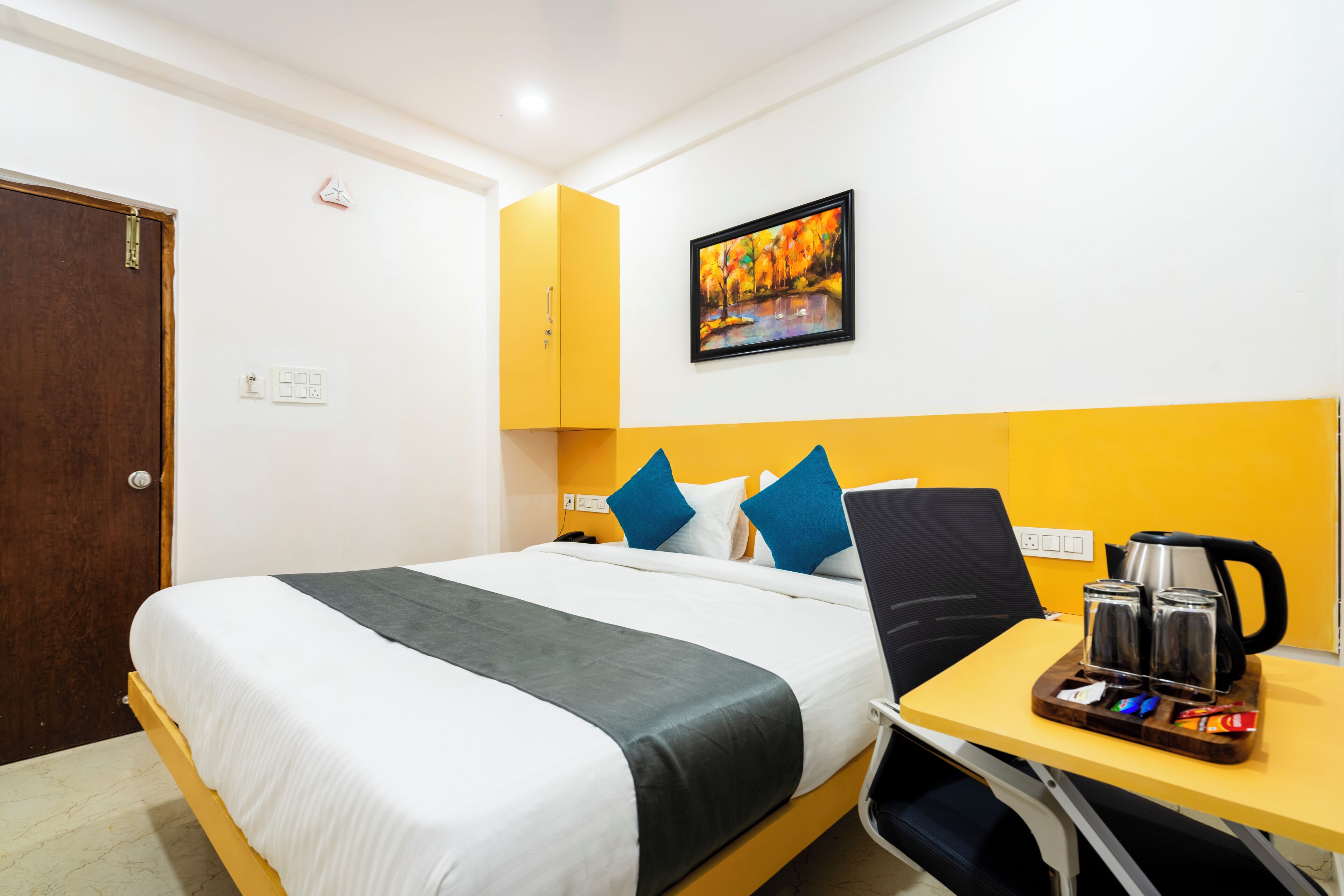 Habitación de hotel con cama, escritorio con cafetera y un cuadro en la pared.