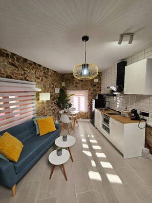 A modern kitchen with white cabinets, a stone wall, a blue sofa with yellow cushions, and a dining area with a table and chairs. - El Mirador, with Terrace and Jacuzzis (Montánchez)