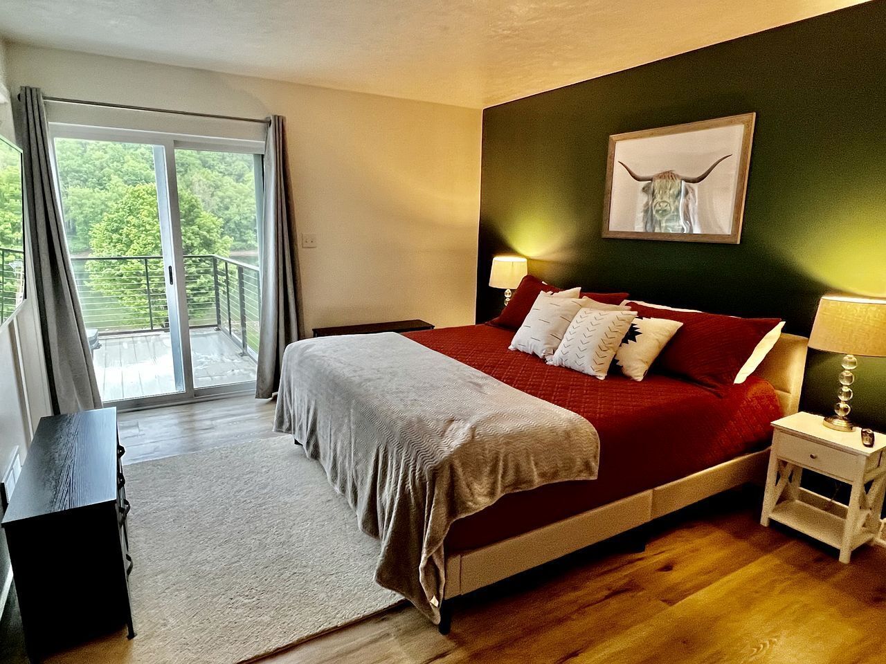 A bedroom with a bed, a nightstand, a lamp, a framed picture on the wall, and a view through a sliding door.