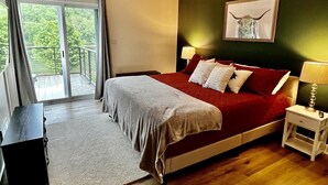 A bedroom with a bed, a nightstand, a lamp, a framed picture on the wall, and a view through a sliding door.