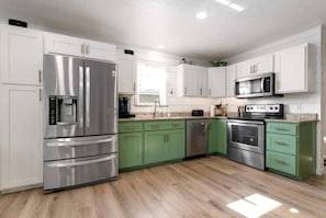A modern kitchen with stainless steel appliances, green cabinets, and a wooden floor.