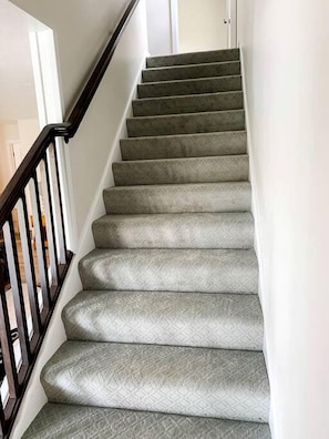 Una escalera con alfombra, barandilla y una puerta al final.