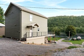 A two-story building with a balcony, a small porch, and a view of a lake and forest. - Family Adventure Awaits: Amazing Cabin by the Allegheny River in Pennsylvania (Parker)