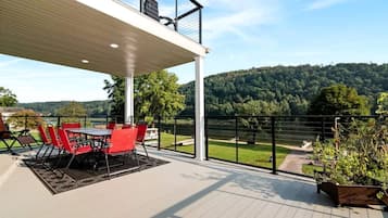 A covered outdoor area with a table and chairs, a view of a lake, and a forested hill in the background.