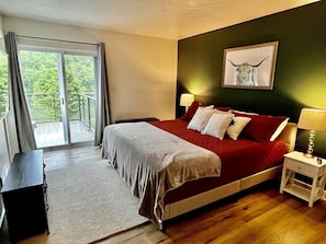 Une chambre à coucher avec un lit, une table de chevet, une lampe, un tableau encadré au mur et une vue à travers une porte coulissante.