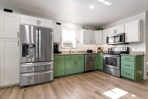 A modern kitchen with stainless steel appliances, green cabinets, and a wooden floor.