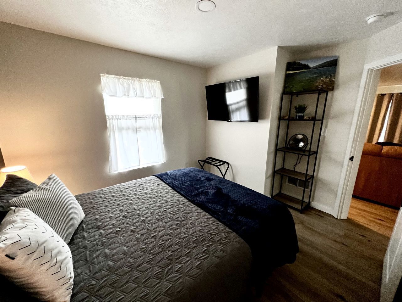 Ein Schlafzimmer mit einem Bett, einem Fernseher, einem Regal mit Dekoration und einem Fenster mit Vorhängen.