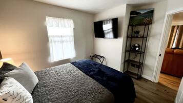 Ein Schlafzimmer mit einem Bett, einem Fernseher, einem Regal mit Dekoration und einem Fenster mit Vorhängen.