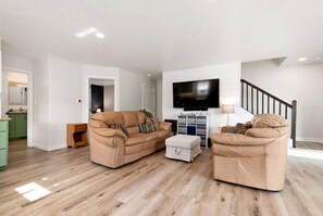 Un salon avec un ensemble de meubles de couleur beige, un téléviseur à écran plat et un escalier.