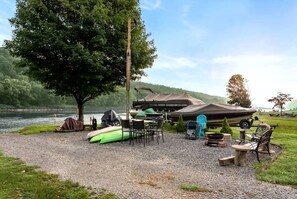 A lakeside campsite with a covered boat storage area, a tent, and a gravel ground.
