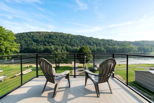 A balcony with two chairs overlooking a river and forested hills.
